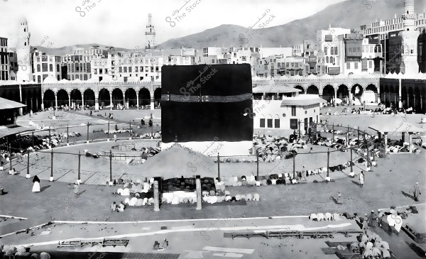 A historical image of the Kaaba, surrounded by worshippers and the old architectural style of the Grand Mosque in Mecca.