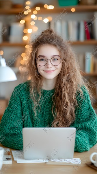صورة لامرأة شابة تجلس في بيئة منزلية دافئة, ترتدي نظارات وكنزة خضراء سميكة. شعرها طويل ومجعد ومصفف بشكل غير مرتب. خلفية الصورة تحتوي على رفوف كتب وزينة بأضواء دافئة تضيف لجواً مريحًا. تجلس أمام جهاز كمبيوتر محمول مفتوح على طاولة خشبية.
