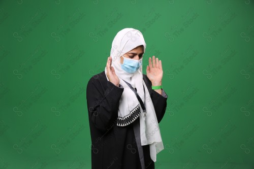 Portrait of a woman with white skin on a green background, wearing a mask and performing the duty of prayer