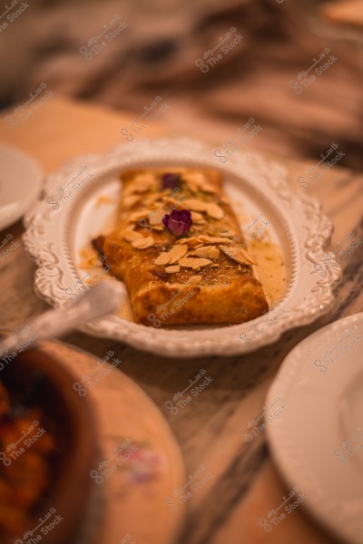 A dish featuring a wrapped dessert garnished with almond slices and a small flower, placed on a decorative ceramic plate.