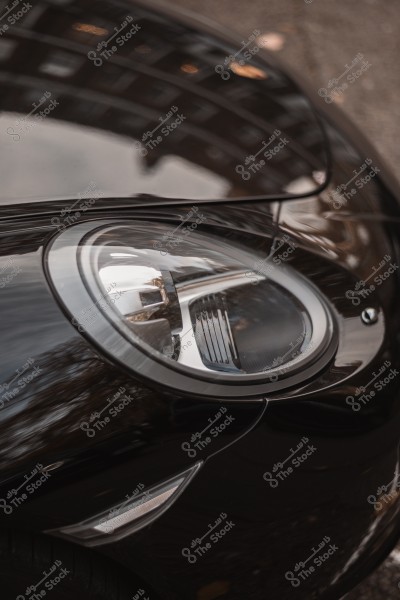 Close-up image of a headlight on a shiny black car, showing its sleek design and light reflection.