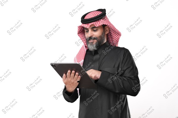 رجل يرتدي الثوب السعودي التقليدي والغترة والعقال, يستخدم جهاز لوحي بإيجابية.