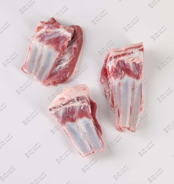 Raw meat pieces placed on a white surface. The image shows three cuts of meat containing bone, with the meat color varying from dark red to pink, accompanied by some white fat.