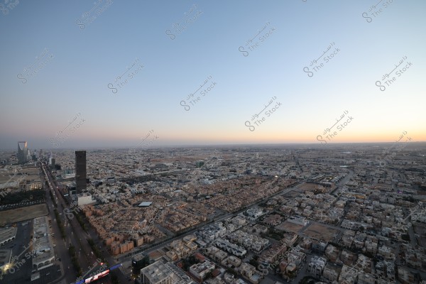 صورة لمنظر جوي لمدينة الرياض في السعودية وقت الغروب. تظهر في الصورة المباني المتراصة والشوارع المنظمة, مع ظهور برج المملكة البارز في الأفق. السماء متدرجة الألوان بين الأزرق والبرتقالي مما يضفي جمالاً على المدينة.