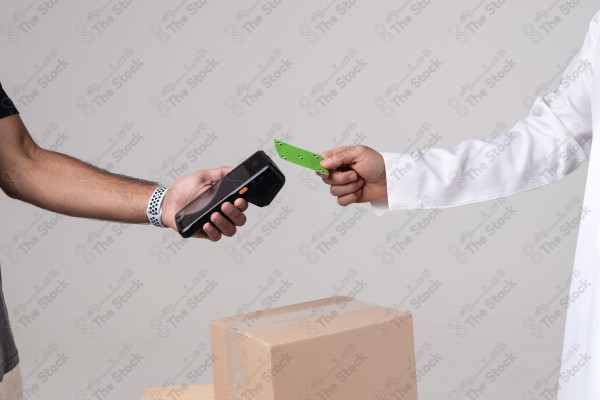 Portrait of a Saudi man holding a card and making automatic payments, with a cardboard next to him on a white background