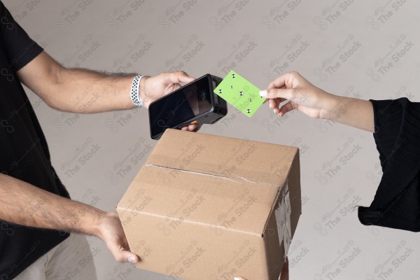 Portrait of a Saudi woman holding a card and making automatic payments, with a cardboard next to her on a white background