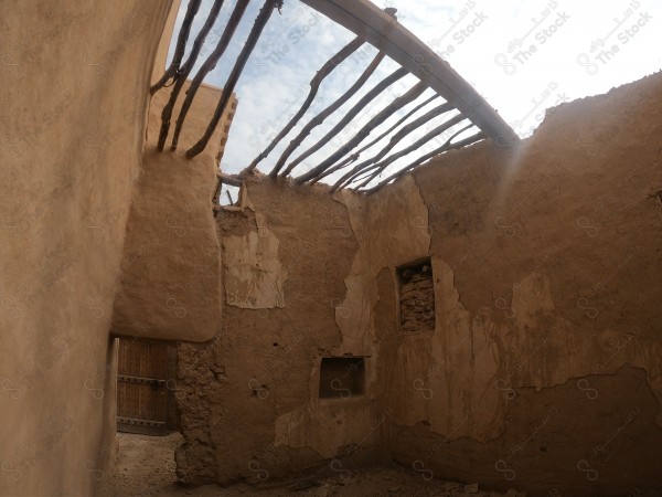 Remnants of an old mud house with a destroyed roof made of wooden branches, a collapsed roof and cracked walls.