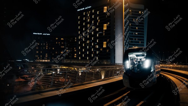 قطار مترو يسير ليلاً بجانب مبنى مضاء في مدينة الرياض.