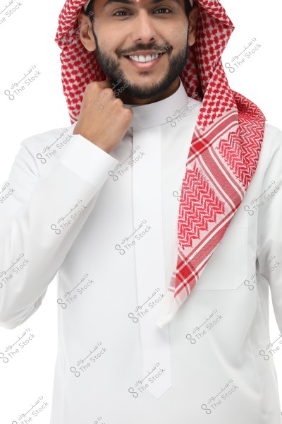 A portrait of a man wearing traditional white thobe with a red and white checkered ghutra and agal. The expression on his face displays a gentle smile, and the clothing suggests it is traditional attire from the Gulf region, such as Saudi Arabia.