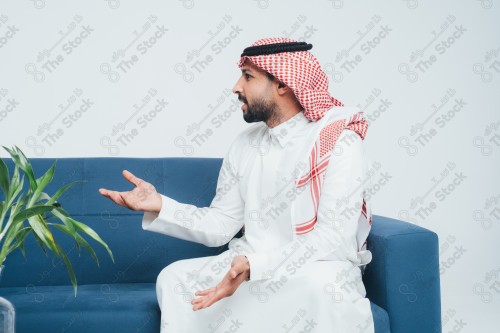 رجل سعودي يتناقش ويقوم بتفاعل بيديه على أريكة زرقاء