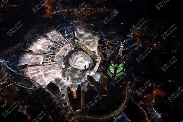 An aerial view of Mecca at night showing the Kaaba and the Grand Mosque beautifully illuminated alongside the Clock Tower.