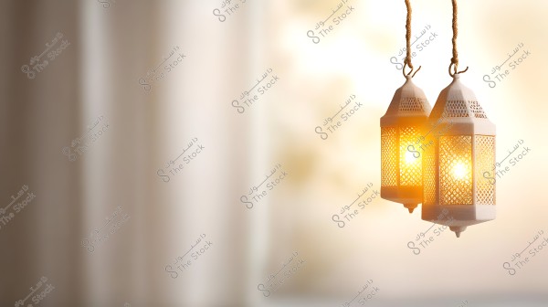 Hanging oriental lanterns with a warm glow, suspended by burlap strings against a softly blurred warm-toned background. The lanterns have a perforated design through which the light shines.