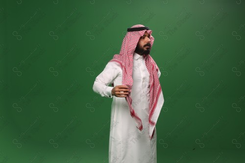 رجل سعودي يقف على خلفية خضراء يرتدي الثوب و الشماغ، يقوم بمسك الشماغ ويعدله ، احتفالات العيد