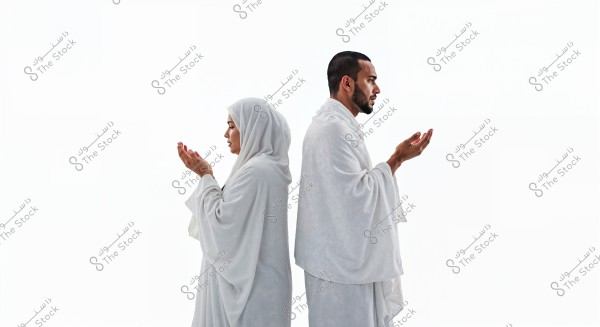 An image of a man and woman standing back to back with their hands raised in prayer. They are wearing white clothing resembling Ihram garments. Their stance reflects a scene from Hajj or Umrah. The background is entirely white, highlighting the details of their devotional attire.