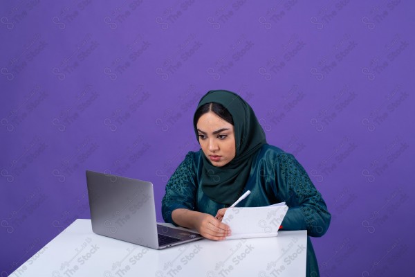 Portrait of a young Saudi woman wearing an abaya and hijab, holding a pen and thinking, against a purple background