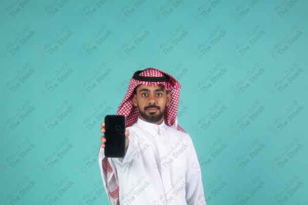 بورتريه رجل سعودي على خلفية تركوازي،  يرتدي الزي السعودي التقليدي ممسك بهاتفه، الاتصالات والتقنية