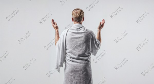 The image shows a man from the back wearing a white bathrobe, with a white towel draped over his shoulder. The man has his arms raised, appearing to be in a state of relaxation or contemplation. The background is a plain white, giving the image a simple and serene appearance.