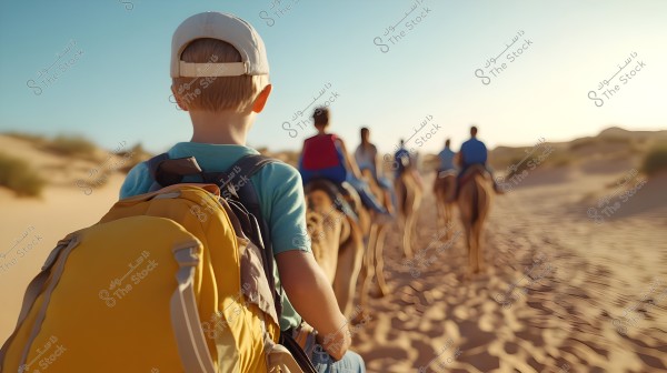 The image shows a child wearing a white cap and carrying a yellow backpack, riding a camel in a desert. In front of him, several other people are also riding camels, suggesting an expedition or adventure in a desert setting. The sky is clear blue and the sand is golden.