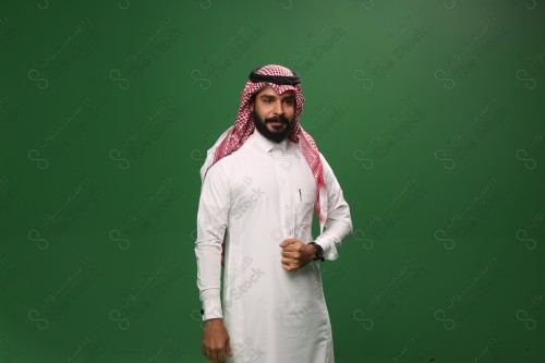 رجل سعودي يقف على خلفية خضراء يرتدي الثوب و الشماغ، يقوم بمسك ثوبه، احتفالات العيد