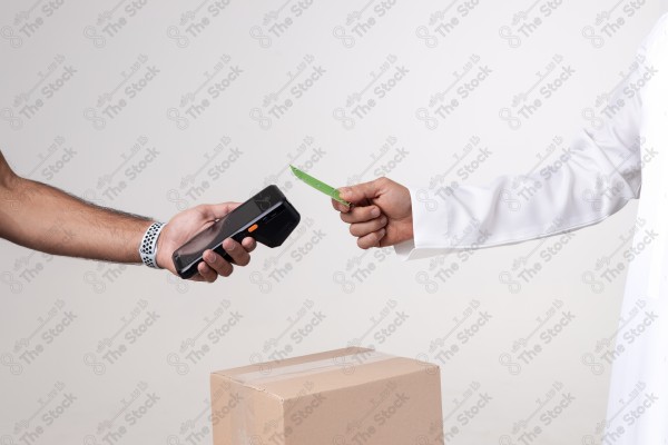 Portrait of a Saudi man holding a card and making automatic payments, with a cardboard next to him on a white background