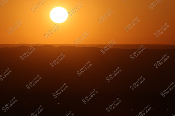 A sunset over a desert landscape, featuring a large, bright sun in the orange sky, with shadow gradients cast over the hills on the horizon.