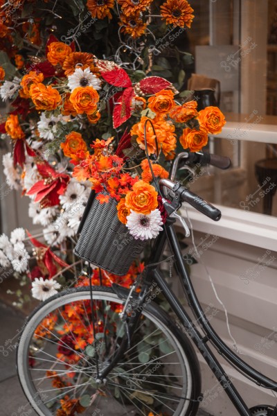 A bicycle decorated with orange and white flowers placed in a front basket, with more colorful flowers in the background.