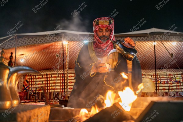 صورة لرجل يرتدي ثوبًا عربيًا تقليديًا وغطاء رأس أحمر وأبيض داخل خيمة مزخرفة بالنقوش. يظهر الرجل وهو يصب القهوة العربية من دلة فضية, ويوجد نار مشتعلة أمامه. الإضاءة الدافئة تضفي جوًا تراثيًا على المشهد.