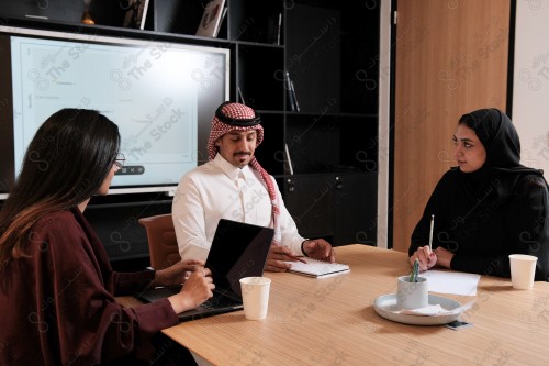 A Saudi man in traditional Saudi dress holds a meeting with Saudi female employees wearing abaya in the meeting room