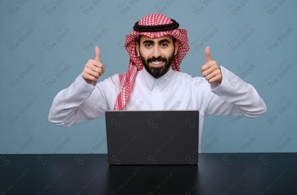 بورتريه شاب سعودي يرتدي الزي السعودي يستخدم جهاز المحمول ويتفاعل معه ، يقف على خلفية سماوية.