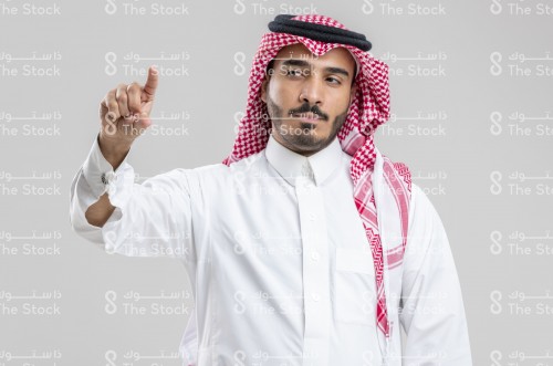 بورتريه رجل سعودي يرتدي الزي السعودي التقليدي يشير بأصابعه السبابة والإبهام يسار الصورة