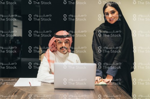 اجتماع عمل بين موظف سعودي يرتدي الثوب وموظفة سعودية ترتدي العباءة في قاعة الاجتماعات