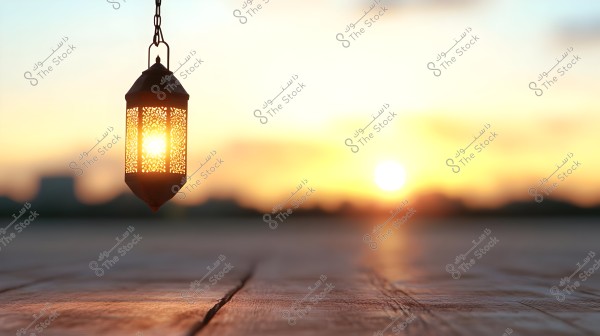 A traditional hanging lantern glowing in the light of a sunset, suspended above a wooden surface with distinct texture. In the background, a distant cityscape is visible with a setting sun casting warm colors to the sky.
