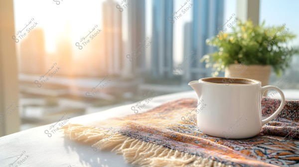 A white teapot containing a hot beverage is placed on a brightly patterned fabric. In the background, there are blurred skyscrapers under the sunlight, with a small green plant in a pot on the right side.