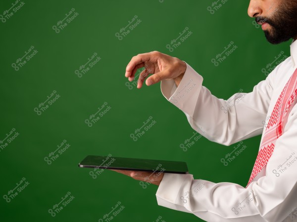 شخص يرتدي الزي الخليجي التقليدي يمسك بجهاز لوحي بيده على خلفية خضراء.