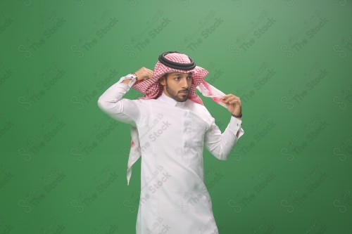 بورتريه رجل سعودي يرتدي الزي السعودي التقليدي يعدل شماغه استعداد للخروج، شاب يتأنق لإحدى المناسبات