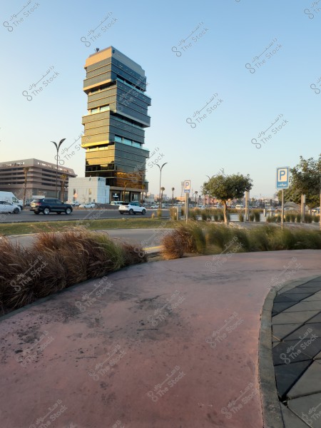 مبنى ذو تصميم حديث ومتعدد الطبقات يعكس ضوء الشمس ويقع بجانب طريق مع سيارات متحركة وأشجار وعلامات مواقف في مقدمة الصورة.

-