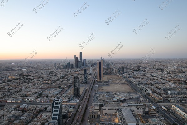 An aerial view of Riyadh, Saudi Arabia, during sunset. The image showcases modern buildings and prominent skyscrapers in the central area, with the city\'s streets stretching out and the urban density visible in the distant horizon.