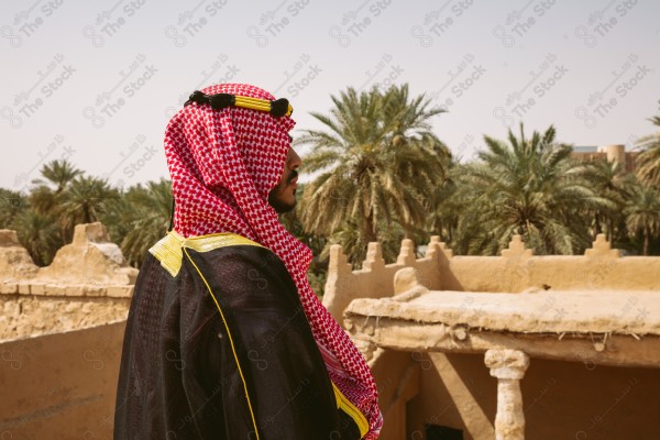 لقطة لرجل سعودي يرتدي الزي التراثي الشعبي في يوم التأسيس يقف فوق مبنى طيني, الزي التراثي, يوم التأسيس, مباني أثريه قديمه.