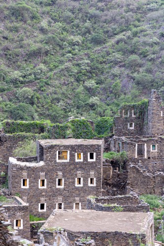 An ancient building built of stones in the middle of a group of windows surrounded by white paint while the sky looks cloudy during sunset, Rijal Almaa Heritage Village in the Asir region