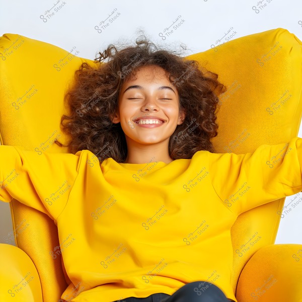 Image of a girl sitting on a yellow chair. She is wearing a yellow sweater and has curly brown hair. She appears to be smiling with her eyes closed, conveying a relaxed and happy demeanor.