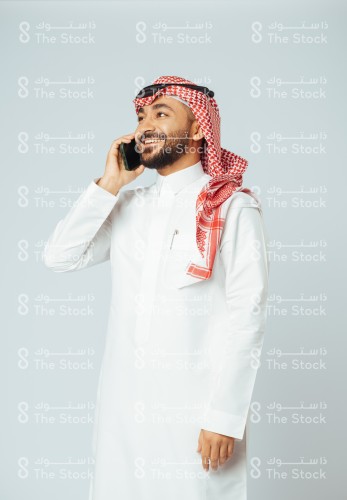 بورتريه رجل سعودي يرتدي الزي السعودي التقليدي يتحدث بالجوال وتظهر عليه السعادة، شاب يجري مكالمة هاتفية