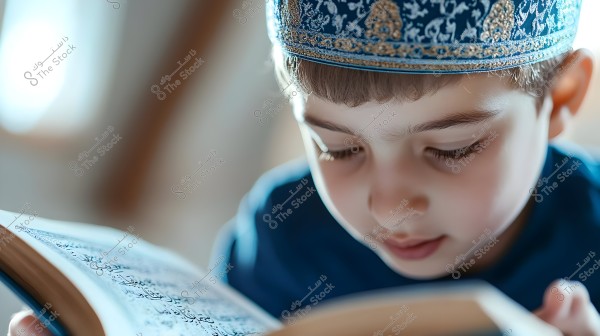 A close-up image of a young boy wearing a traditional blue and gold patterned cap, reading a book in Arabic. The focus is on the boy\'s face and the book, which features text in Arabic.