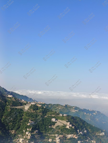 منظر طبيعي يوضح سلسلة من الجبال الخضراء المنتشرة بالمباني الصغيرة على سفوحها. السماء زرقاء صافية, ويمكن رؤية بعض الغيوم البيضاء في الأفق فوق الجبال.