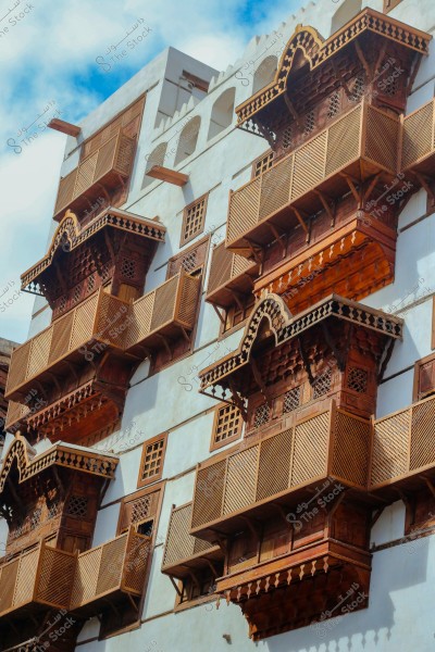 An image of a traditional building facade featuring distinctive wooden balconies designed in the Hijazi architectural style in Saudi Arabia. The balconies are intricately carved and project from the white walls, reflecting the traditional architectural style of the region. The sky is blue in the background.