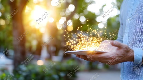 The image shows hands holding a tablet, from which golden, sparkling light reminiscent of magical sparks flows out. The blurred background features warm sunlight filtering through green trees, conveying a sense of hope and modernity.