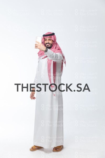 بورتريه رجل سعودي يرتدي الثوب يبتسم وهو يلتقط سيلفي بجواله