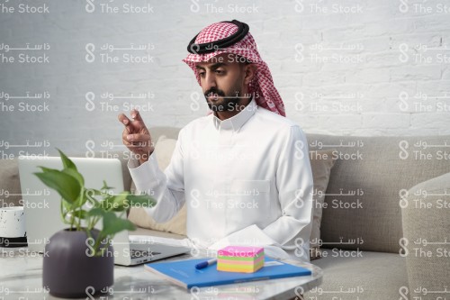 رجل سعودي يرتدي الزي السعودي الرسمي يجلس أمام جهاز الأبتوب يتحدث مع أحدهم بلغة الإشارة