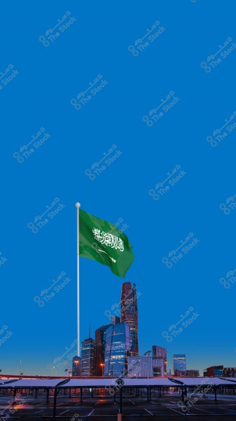 An image depicting a city skyline in Saudi Arabia with the national green flag waving in the foreground. Modern tall buildings are visible in the background under a clear blue sky.\r\n\r\n####