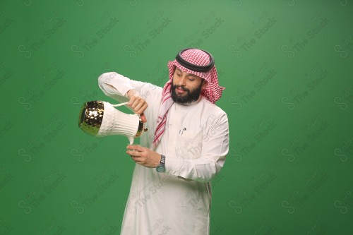 شاب سعودي على خلفية خضراء يرتدي الثوب و الشماغ، يقوم بعمل حركات بيده، يصب القهوه السعودية، احتفالات العيد