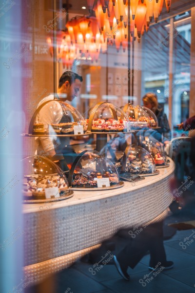 A pastry shop displaying a variety of cakes under glass covers, with a person standing behind the counter.